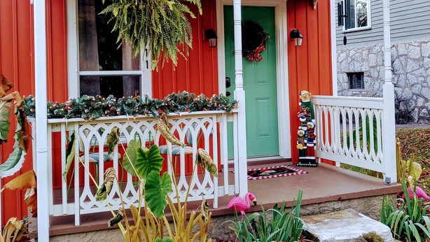 Ein rotes Haus mit einer grünen Tür, einer Veranda mit weißem Geländer und einem Kranz an der Tür.