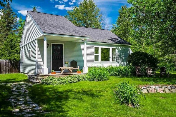 A small, single-story house with a porch, a stone pathway leading to the front door, and a well-maintained lawn.