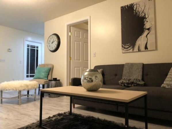 Un salon avec un canapé, une table basse, une horloge et un tableau au mur.