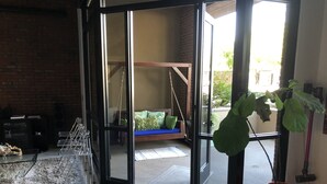 Una stanza con una porta vetrata che dà sull'esterno, una poltrona a dondolo, una pianta grande e un tavolino con un vaso.
