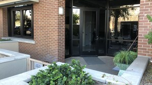 Un edificio in mattoni con un ingresso in vetro, una piccola area giardino con piante e un cartello che indica divieto di accesso.