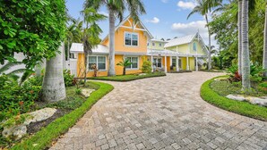 A yellow house with a paved driveway, surrounded by palm trees and greenery. - Cozy Retro Cottage located less then 2 blocks from the Gulf Beach - Heated Pool in Private Oasis! (Holmes Beach)