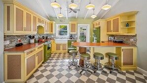 A kitchen with yellow cabinets, a checkered floor, a central island with stools, and pendant lights. - Cozy Retro Cottage located less then 2 blocks from the Gulf Beach - Heated Pool in Private Oasis! (Holmes Beach)