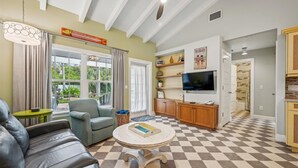 A living room with a checkered floor, a sofa, a chair, a television, and a ceiling fan. - Cozy Retro Cottage located less then 2 blocks from the Gulf Beach - Heated Pool in Private Oasis! (Holmes Beach)