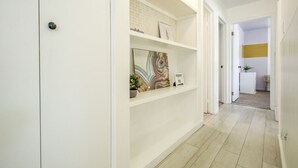 Un corridoio con pareti bianche, una porta e uno scaffale con una pianta e un quadro incorniciato.