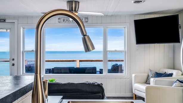 Ett kök med en diskho i rostfritt stål, ett böjt blandare och utsikt över havet genom stora fönster.