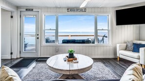 Ett rum med utsikt över stranden, en takfläkt, en TV och en skylt med texten ”Strandstuga”.