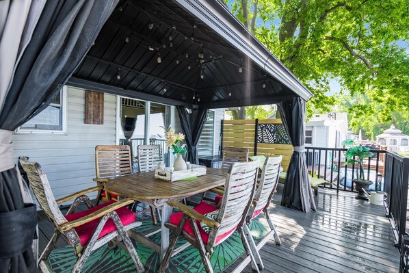 Un espace extérieur abrité, avec une table et des chaises en bois, un pot de fleurs et une vue sur un quartier résidentiel.