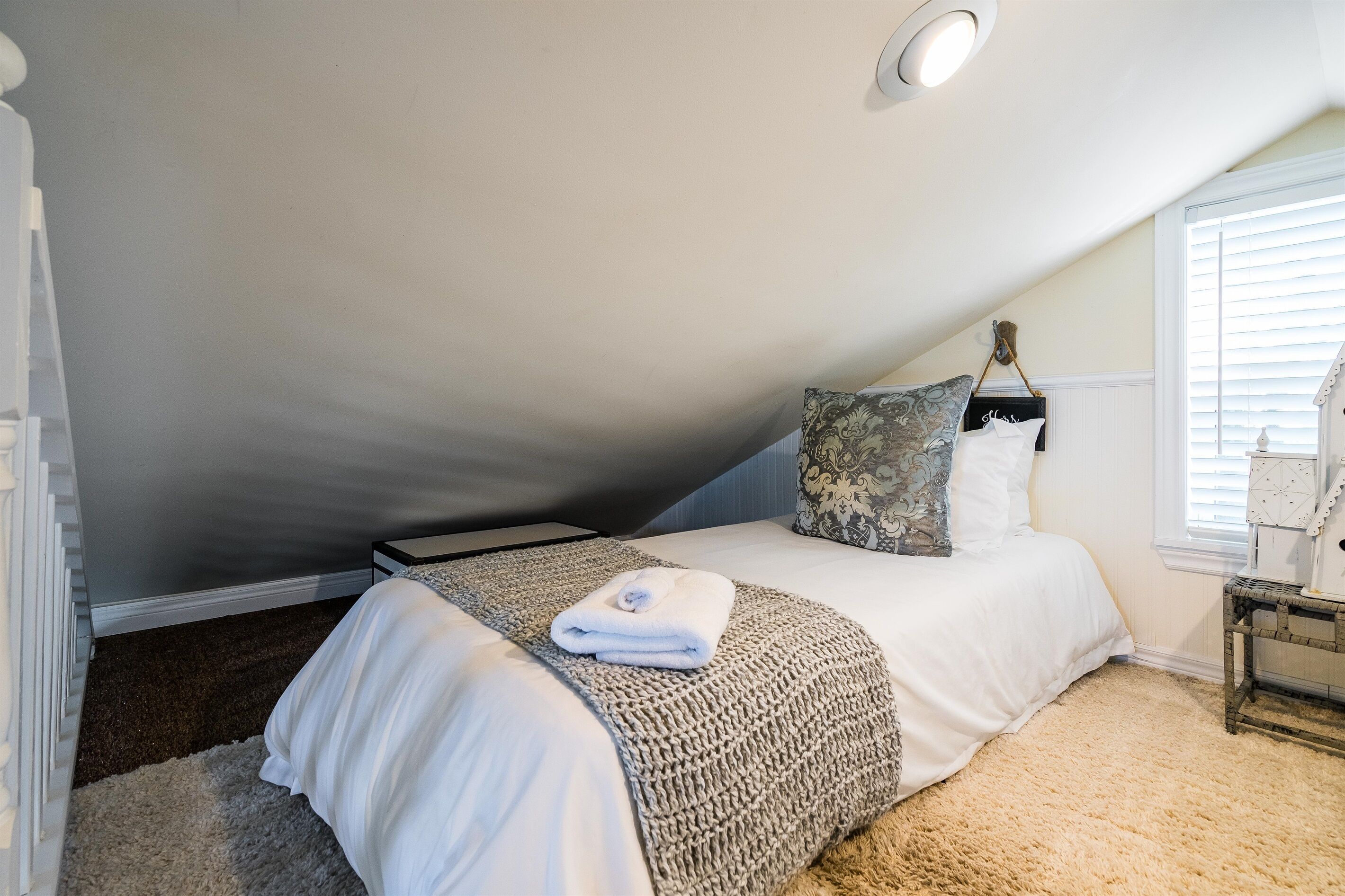 Una camera da letto con un letto, un comodino, una finestra con persiane e una lampada a soffitto.