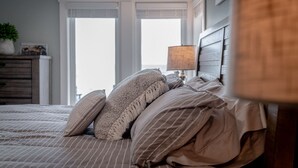 Un lit bien fait, avec une literie à rayures et un plaid en tricot, une tête de lit en bois et une lampe sur une table de chevet.