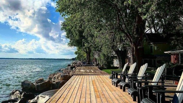 Une jetée en bois s’étendant dans une étendue d’eau, bordée de chaises Adirondack et entourée d’arbres.