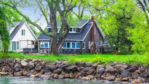 A lakeside cabin with a deck and a large tree in front.