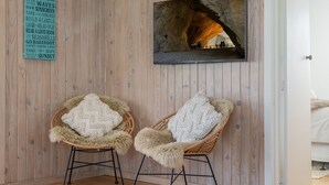 Una habitación con paredes de paneles de madera, dos sillones de mimbre con cojines mullidos, un cuadro con una cueva y un cartel con palabras relacionadas con la playa.