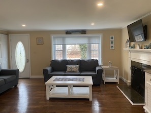 A living room with a dark grey sofa, a white coffee table, a fireplace, and a TV mounted above it.