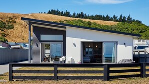 A modern two-story house with large windows, a flat roof, and a view of a hilly landscape. - The Kaikoura Bach Retreat (Kaikoura)