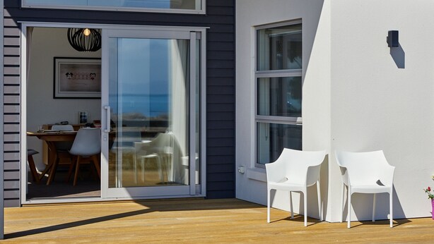 A modern house with a sliding glass door leading to a patio area. - The Kaikoura Bach Retreat (Kaikoura)
