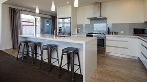 A modern kitchen with a central island, stainless steel appliances, and bar stools. - The Kaikoura Bach Retreat (Kaikoura)