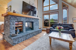 A modern living room with a stone fireplace, a large TV mounted above it, and a black leather couch.