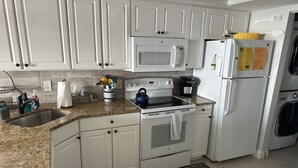 Une cuisine moderne avec des armoires blanches, un comptoir en granit, un four à micro-ondes, une cuisinière et un réfrigérateur.