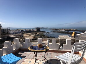 Een terras met een tafel en stoelen met uitzicht op een kustgebied met rotsachtig terrein en een zeezicht.