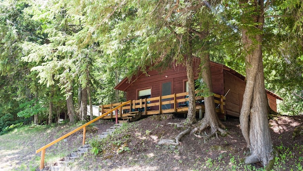 A wooden cabin with a wooden staircase leading up to it, surrounded by trees.