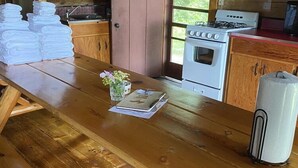 A wooden table with towels, a notebook, and a thermos in a cabin-style kitchen with wooden cabinets and a stove.