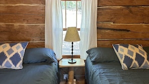 A cabin room with two beds, a window with curtains, and a table lamp.