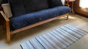 Een houten blokhut inrichting met een houten bank, een kleine tafel met een lamp en een raam met gordijnen.