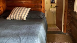 Een slaapkamer in een blokhut met een bed, een gestreept kussen en een houten deur naar een badkamer.