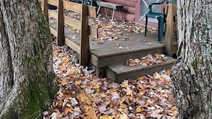 Una cabaña rústica con una terraza de madera, un letrero que dice "KOLME" y algunas sillas de plástico afuera.