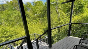 A wooden deck with wicker chairs and a metal railing, overlooking a forested area.