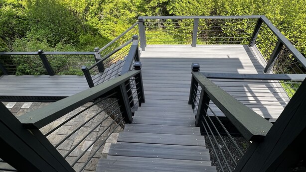 A wooden bridge with metal railings leading to a forested area.