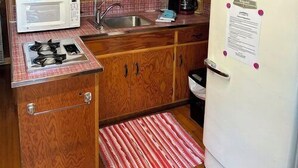 Una cucina compatta con mobili in legno, un forno a microonde bianco, un piano cottura a gas, un lavandino e un frigorifero bianco.