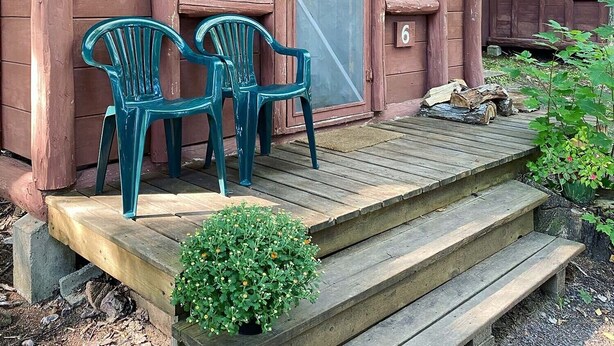Un rustico chalet con un portico in legno, due sedie di plastica e una piccola pianta in vaso.
