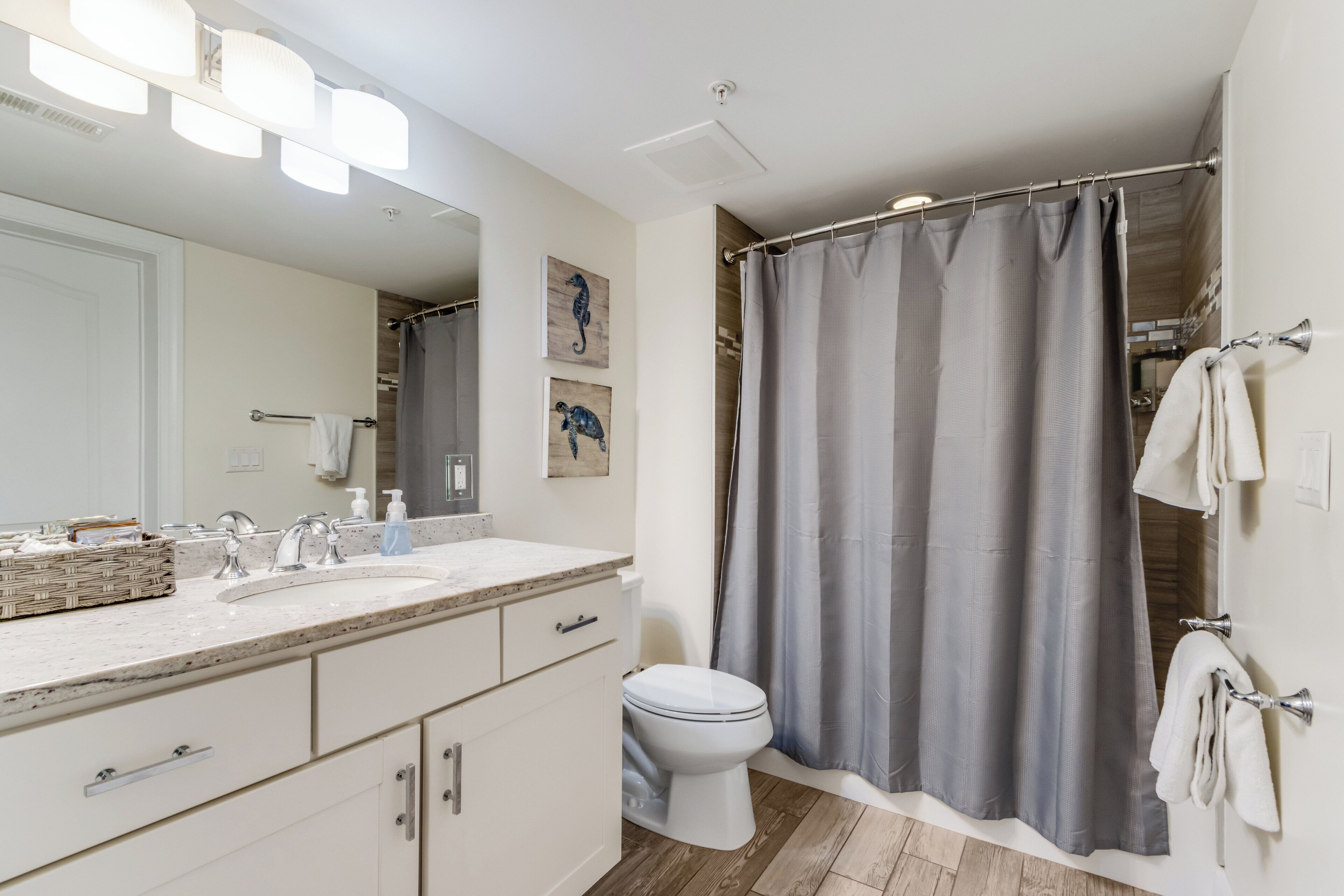 A bathroom with a large mirror, two sinks, a toilet, and a shower curtain.