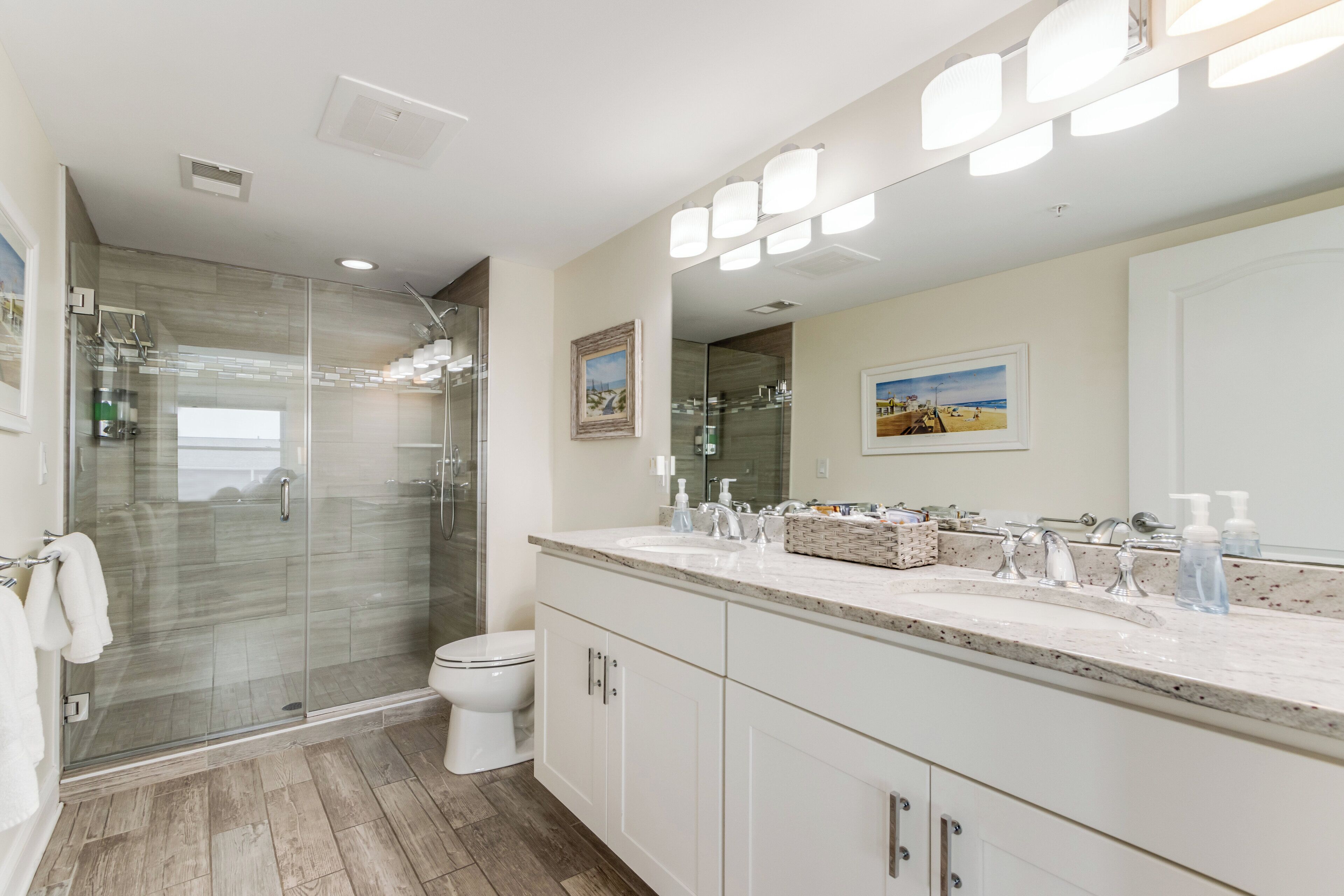 A modern bathroom with a glass-enclosed shower, a large mirror, and a vanity with a marble countertop.