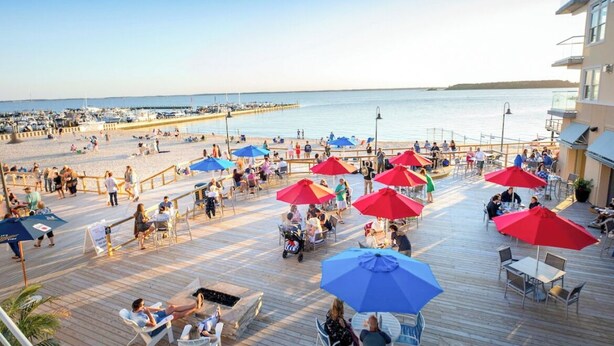 A beachside deck with outdoor seating and umbrellas, overlooking the beach and water. - Luxury water-view condo with high-end finishes and beach toys included! (Dewey Beach)