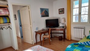 A bedroom with a bed, a desk with a computer, a chair, a radiator, and a window with curtains.