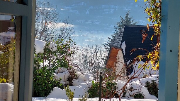 A view through a window of a building with a snow-covered landscape, mountains, and a clear sky.