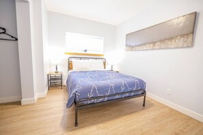 Quarto com cama, mesa de cabeceira, janela e obra de arte na parede.