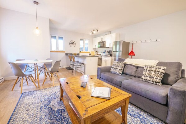 Uma sala de estar moderna com um sofá cinza, uma mesa de centro de madeira e um tapete azul estampado.