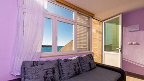 A room with a sofa, a window with blinds, and a view of the sea.