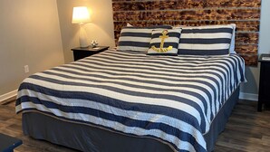 Un letto rifatto con biancheria a righe, una testiera in legno e una lampada da comodino.