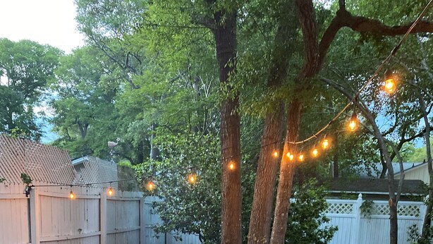Patio esterno con pavimento in pietra, un braciere e luci a stringa.