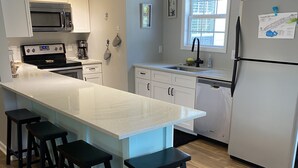 Una cucina moderna con isola centrale, sgabelli da bar, frigorifero e lavastoviglie.