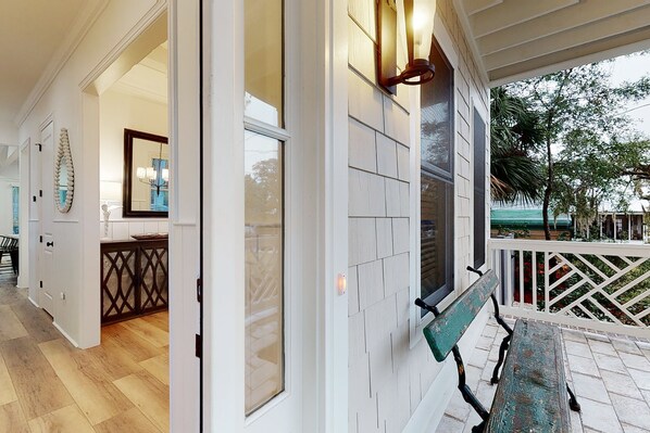A wooden deck with a bench, a white exterior wall, and a view of the outdoors.