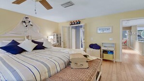Un dormitorio con cama, dosel, mesita de noche, maleta y puerta que da a otra habitación.