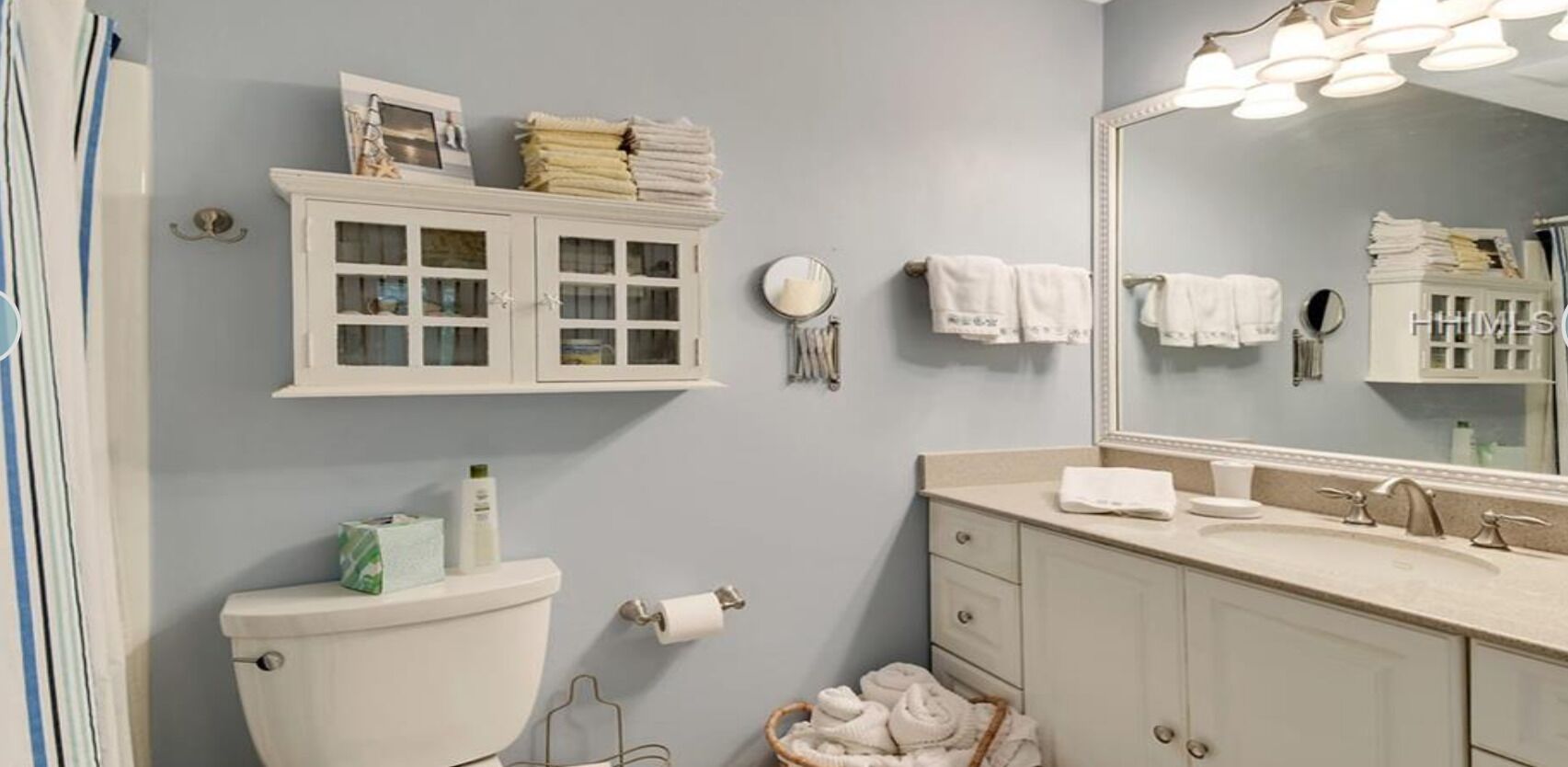 A bathroom with a toilet, a sink with a mirror, a cabinet with towels, and a wall-mounted light fixture.