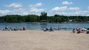 A sandy beach with people relaxing and swimming in the water. - Kawartha Lakes Cottage (Lakefield)