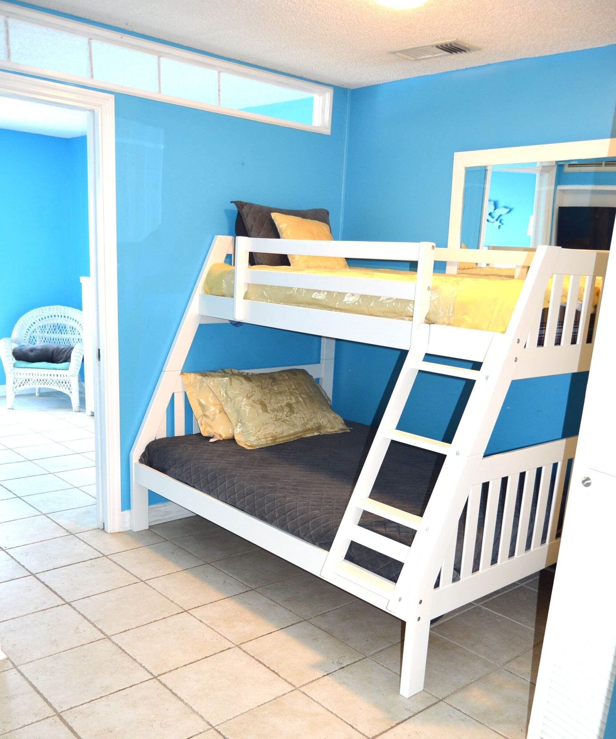 A bunk bed with a ladder, a white chair, and a blue wall.